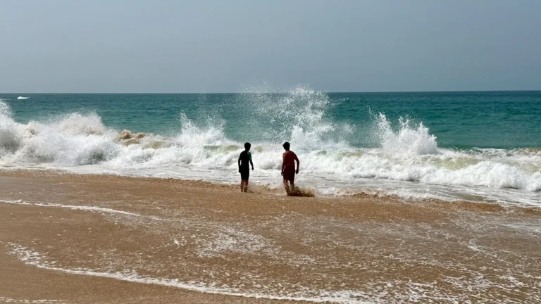 Badende Personen am Strand mit hoher Brandung und Rettungsschwimmern im Hintergrund.