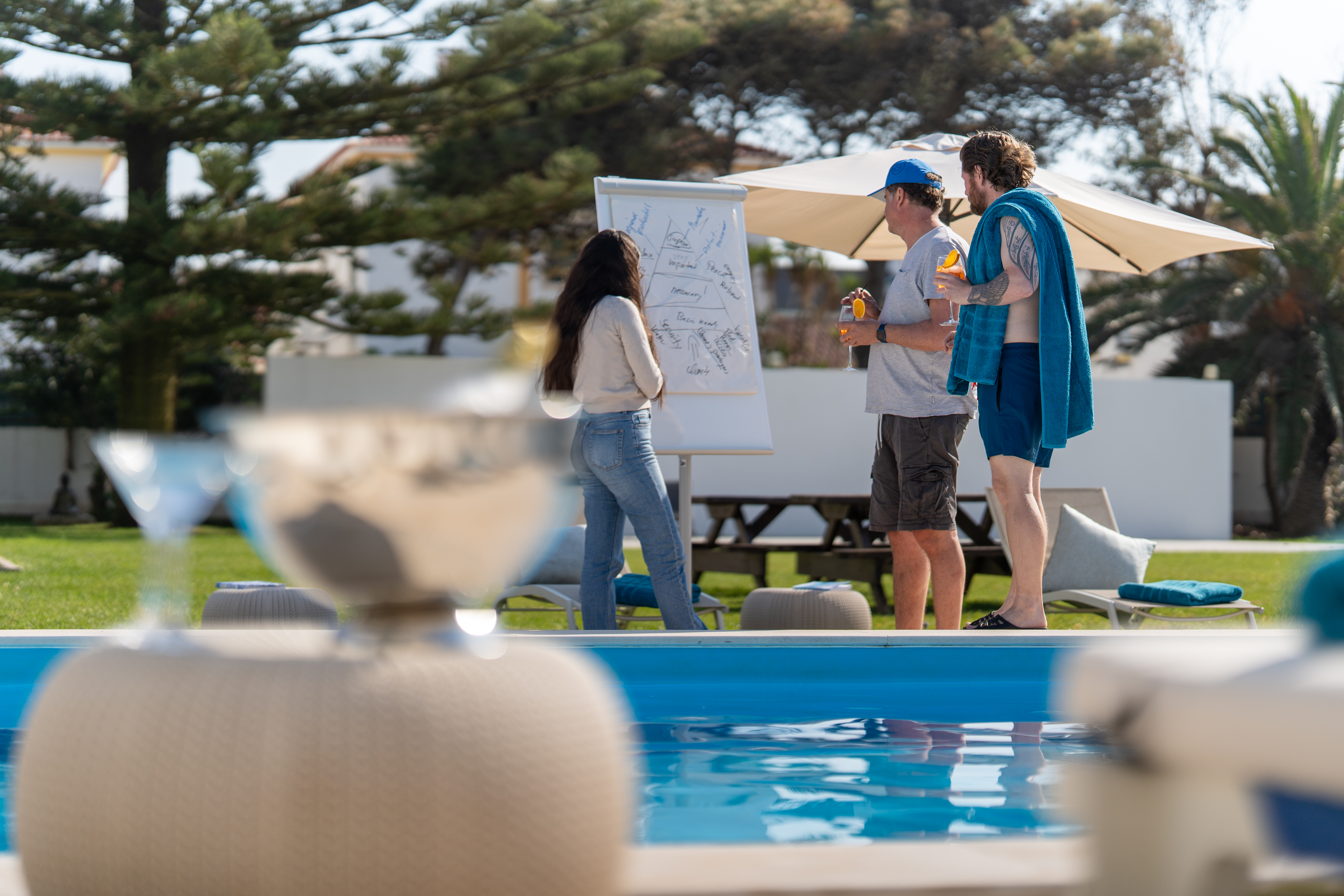 Zwei Männer und eine Frau stehen neben dem Pool vor einem Flipchart und sammeln Ideen während ihrer Workation in Portugal.