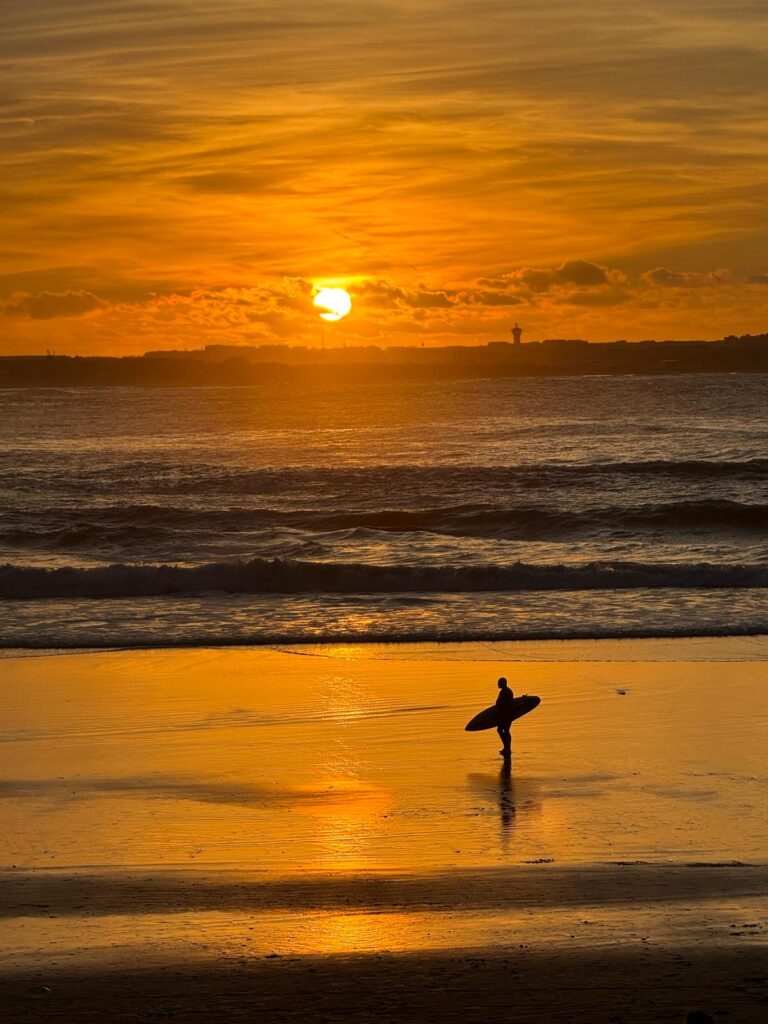 Ein Mann genießt die Workation in Portugal beim Surfen im Sonnenuntergang.