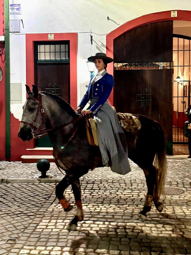 Eine Frau mit traditionellem portugiesischen Reitergewandt sitzt auf einem Pferd und reitet durch die Gassen von Golega.