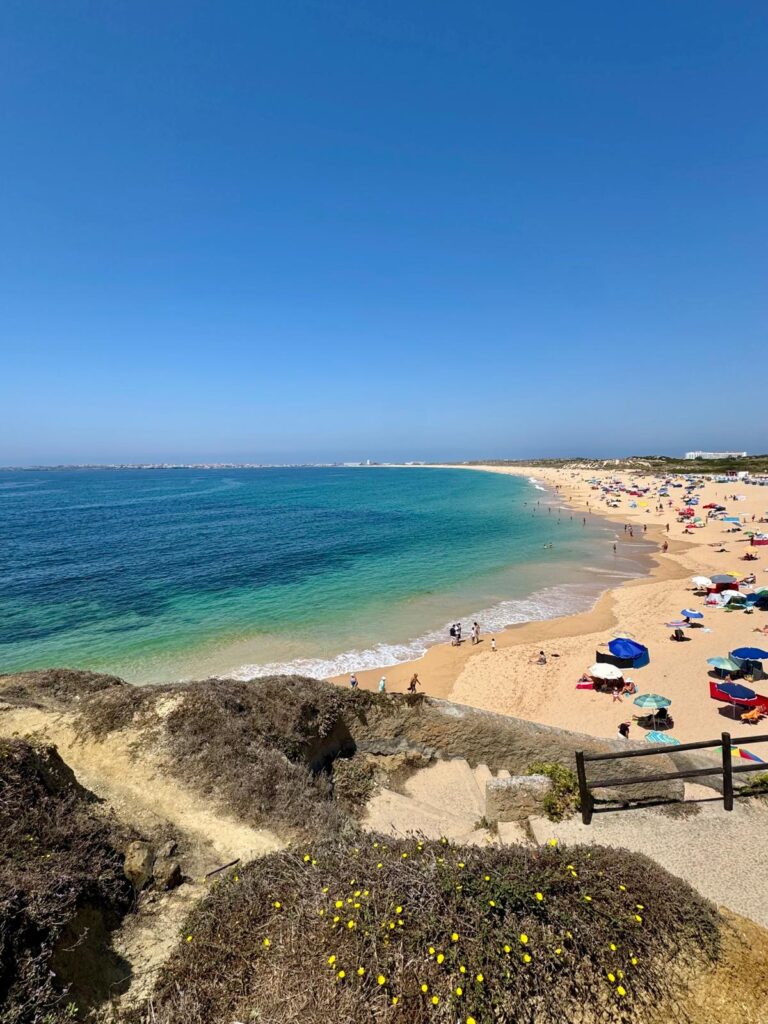 Große Bucht mit Sandstrand, blauem Wasser und Sonnenschirmen bei Peniche.