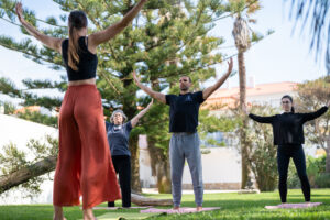 Die Gruppe des Qigong Retreats in Portugal steht gemeinsam im Garten und öffnet die Arme zum Himmel bei einer Qigong-Übung.
